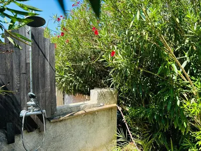 a shower with a hose next to a bush with red flowers at A Pineta in Porticcio