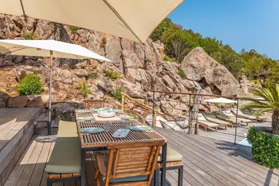 a table with chairs and an umbrella on a wooden deck at Villa Elsa Di Palombaggia in Porto-Vecchio