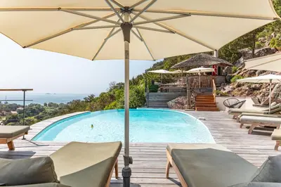 a pool with chairs and umbrellas next to a swimming pool at Villa Elsa Di Palombaggia in Porto-Vecchio