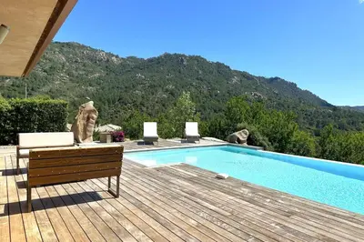 a swimming pool on a wooden deck with a mountain at Villa Taglio Rosso Di Santa Lucia in Sainte-Lucie de Porto-Vecchio