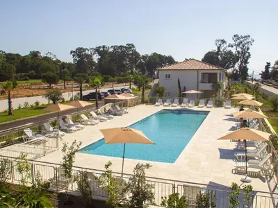 a pool with umbrellas and chairs and a building at Apartment A Suara Linda-2 by Interhome in Ghisonaccia