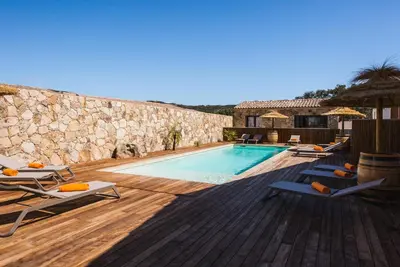 a swimming pool with lounge chairs and a stone wall at Résidence Petra d'Oro - Villa Chiappa in Porto-Vecchio