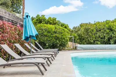 a row of chairs with an umbrella next to a swimming pool at Villa Bella Vista Di Pinarello in Sainte-Lucie de Porto-Vecchio