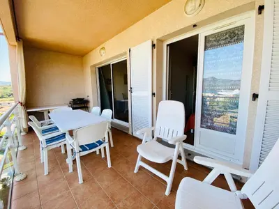 a balcony with white chairs and a table and a window at A Funtana deux chambres, vue mer, piscine et tennis in Propriano