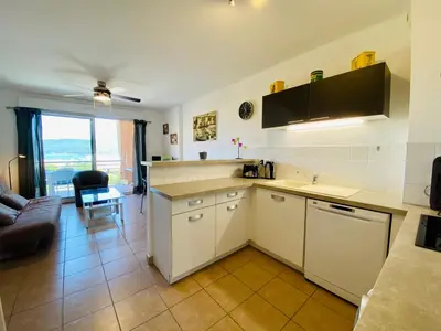 a kitchen with white cabinets and a living room at A Funtana deux chambres, vue mer, piscine et tennis in Propriano