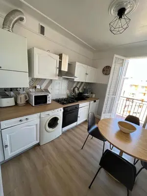 a kitchen with white cabinets and a table and a dining room at Appartement climatisé F3 proche plage port et aéroport in Ajaccio