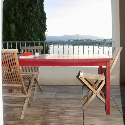 a red table and chairs on a balcony with a view of the water at Les Salins in Porto-Vecchio