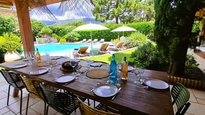 a wooden table with plates and wine glasses next to a pool at Villa Lucendiluna 10 personnes piscine 5 min plage en voiture in Sainte-Lucie de Porto-Vecchio