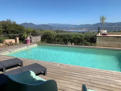 a large swimming pool with a wooden deck and chairs at Villa vue mer 4 chambres in Olmeto
