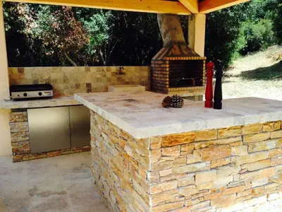 an outdoor kitchen with a stone counter with a fireplace at Villa piscine Sagone Paradise avec magnifique vue mer in Sagone