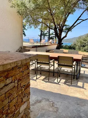 a patio with a table and chairs and a stone wall at Villa piscine Sagone Paradise avec magnifique vue mer in Sagone