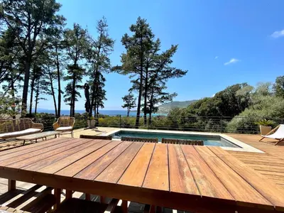 a wooden deck with a pool and chairs and trees at Villa piscine Sagone Paradise avec magnifique vue mer in Sagone