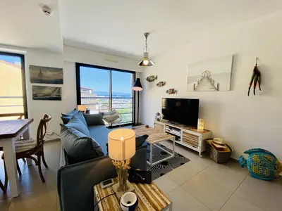 a living room with a couch and a television at Coté Plage pied dans l'eau vue mer in Propriano
