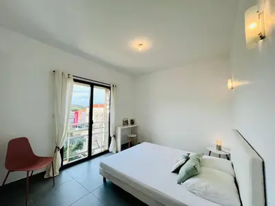 a white bedroom with a bed and a window at Jardins de Quatrina centre ville in Propriano