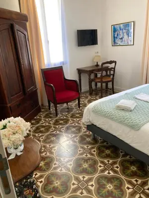a bedroom with a bed and a chair and a table at Hôtel La Demeure Coloniale in Moriani Plage