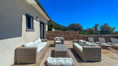 a patio with wicker chairs and a couch and a table at Tres belle villa neuve vue mer avec piscine chauffee in Sainte-Lucie de Porto-Vecchio