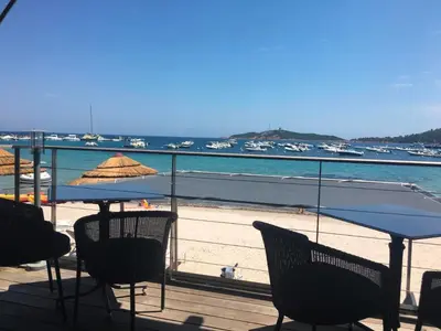 a deck with chairs and an umbrella and the beach at La corse les pieds dans l'eau in Sainte-Lucie de Porto-Vecchio