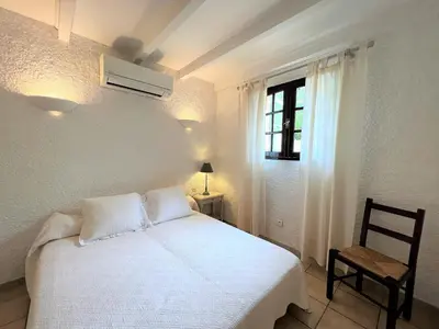a bedroom with a white bed with a chair and a window at Résidence Marie Diane - Appart vue mer et piscine G in Propriano