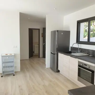 a kitchen with a stainless steel refrigerator and wooden floors at Villa Le Figuier 6 pers piscine chauffée 2 min plage en voiture in Sainte-Lucie de Porto-Vecchio