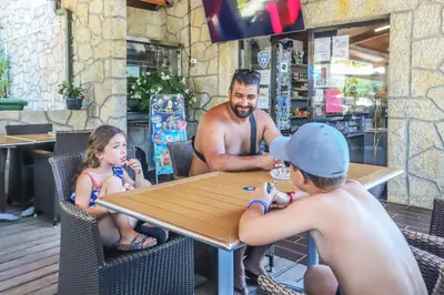 a man and two children sitting at a table at Camping maeva Escapades Colomba in Olmeto