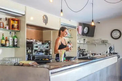 a woman standing behind a counter in a bar at Camping maeva Escapades Colomba in Olmeto