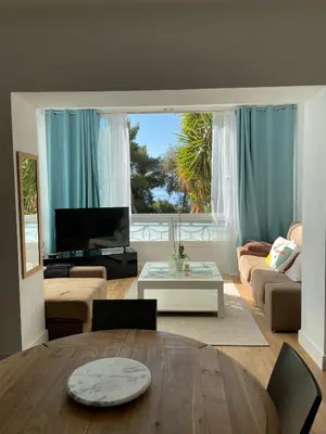 a living room with a table and a large window at Appartement neuf, 2 chambres, climatisé, route des Sanguinaires in Ajaccio