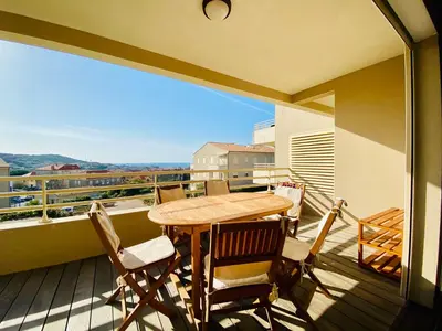 a balcony with a wooden table and chairs at Les Jardins de Quatrina 2 chambres vue mer in Propriano
