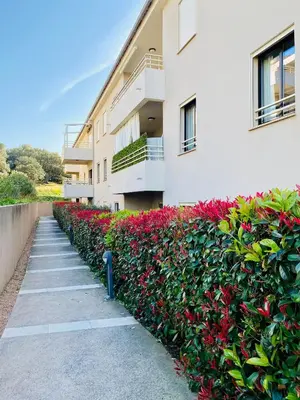 a building with a hedge of red flowers next to a sidewalk at Les Jardins de Quatrina 2 chambres vue mer in Propriano