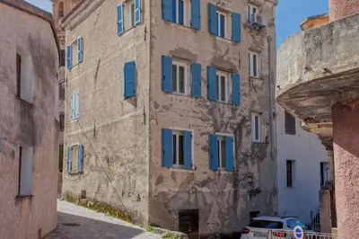 an old building with blue shutters in an alley at Casa Torra in Omessa
