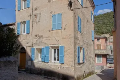 an old building with blue shutters on a street at Casa Torra in Omessa