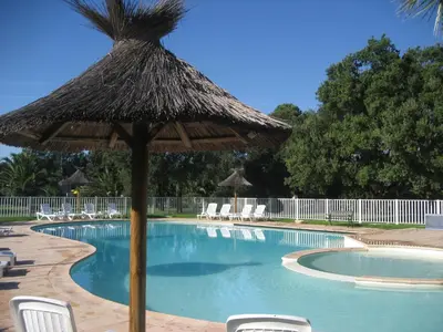 a swimming pool with a straw umbrella and chairs at Liflosa in Lecci