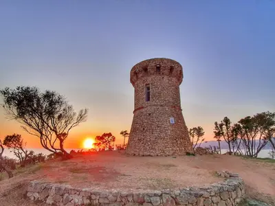 a lighthouse on a hill with the sunset in the background at Les Rivages de Stagnola Appartement T3 vue mer et montagne plage 200m climatisé in Pietrosella
