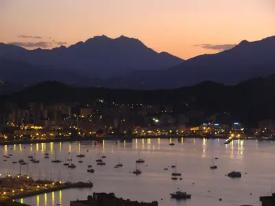 a city with boats in the water at sunset at F3 FENETRE SUR JARDIN VUE MER ET MONTAGNE pour 4 VOYAGEURS in Ajaccio