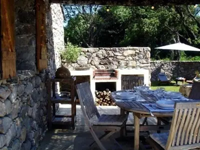 a table and chairs in a yard with a stone fireplace at Les Bergeries de Piazzagina in Piediquarciu