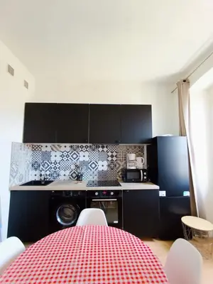a kitchen with black cabinets and a red checked table at Magnifique Grand 30m2 refait à neuf en 2025 lumineux 4 couchages hyper centre Corte 13 cours paoli wifi tv lave linge in Corte
