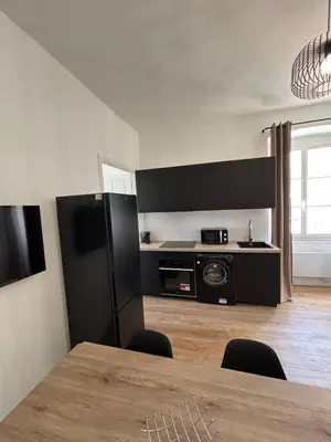 a kitchen with a table and a black refrigerator at Magnifique grand T3 refait à neuf en 2025 plein centre corte 13 cours paoli wifi écran plat lave linge 6 couchages in Corte