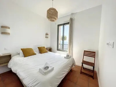 a bedroom with a white bed with a chair and a window at Résidence Eole in Cargèse
