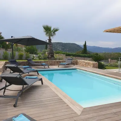 a large swimming pool with chairs and an umbrella at Villa Maria 12 pers piscine chauffée 5 min plage en voiture in Sainte-Lucie de Porto-Vecchio