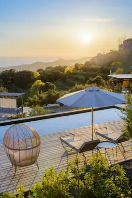 a patio with an umbrella and chairs on a deck at Terre de Maquis, maison d'hôtes vue mer Corse in Sari-dʼOrcino