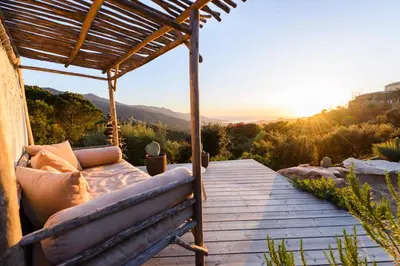 a couch sitting on a wooden deck with the sunset at Terre de Maquis, maison d'hôtes vue mer Corse in Sari-dʼOrcino