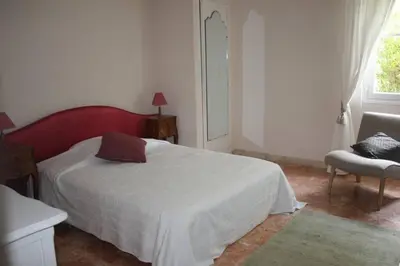 a bedroom with a bed and a chair and a window at Grande maison au cadre verdoyant au centre village in Cargèse