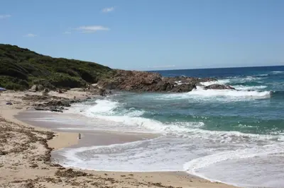 a beach with people walking on the sand and the ocean at Grande maison au cadre verdoyant au centre village in Cargèse