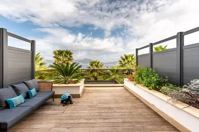a patio with a blue couch on a wooden deck at Les Jardins de la Palmeraie - Sublime vue sur la baie dAjaccio in Porticcio