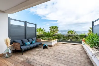 a balcony with a couch and a view of the ocean at Les Jardins de la Palmeraie - Sublime vue sur la baie dAjaccio in Porticcio