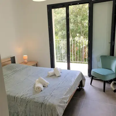 a bedroom with a bed and a blue chair and a window at Villa Leku Lucia 8 pers piscine chauffée 15 min plage en voiture in Sainte-Lucie de Porto-Vecchio