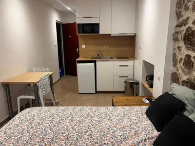 a bedroom with a bed and a table and a kitchen at Charmant studio au cœur de la rue Fesch d'Ajaccio in Ajaccio