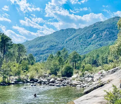 a person swimming in a river with mountains in the background at Résidence Costa Nera Santa Giulia in Porto-Vecchio