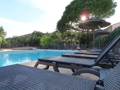 a group of chairs and an umbrella next to a swimming pool at Les Villas de la Résidence U Veniqui in Favone