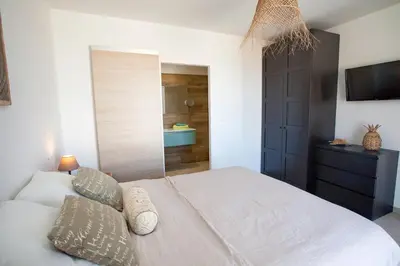 a bedroom with a white bed with pillows and a television at Les Villas de la Résidence U Veniqui in Favone
