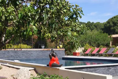 a woman sitting on a bench next to a swimming pool at Les Jardins De Santa Giulia - Charmante chambre dhte in Porto-Vecchio